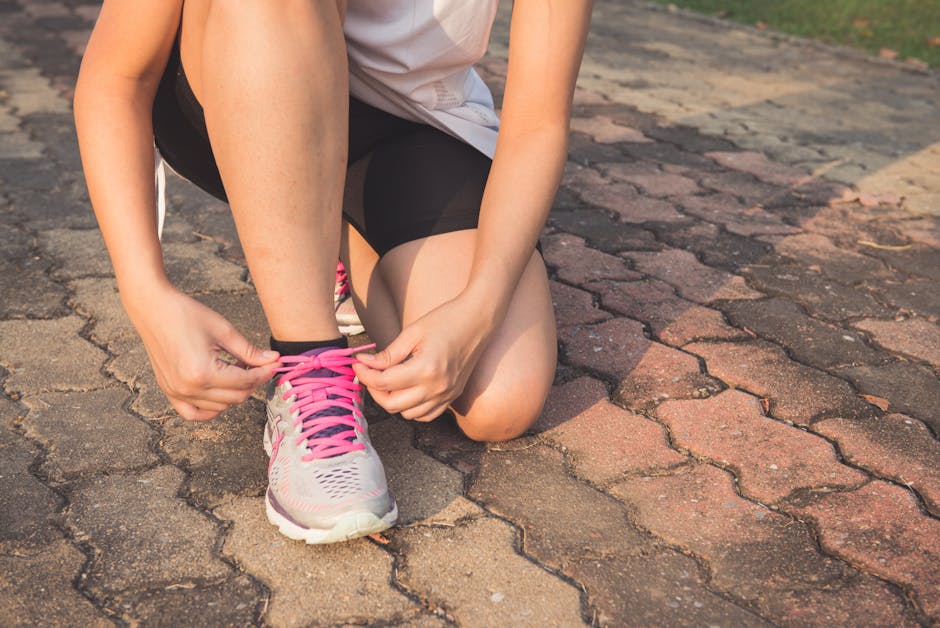 Adult woman tying pink laces on running shoes outdoors. Focuses on fitness and lifestyle