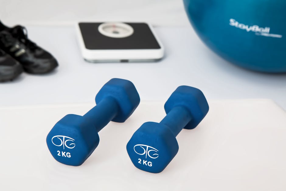 Blue dumbbells placed on a white surface with fitness equipment in the background